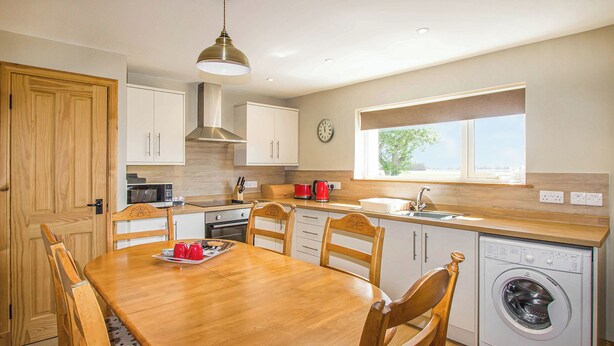 A compact kitchen with a dining table, chairs, a washing machine, and a window with a view. - 3 bedroom accommodation in Portmahomack, near Tain (Portmahomack, near Tain)