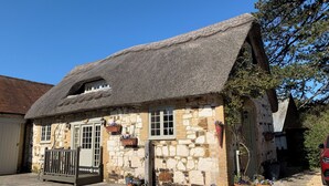A stone building with a thatched roof, stone walls, and hanging flower baskets. - 1 bedroom accommodation in Brighstone, near Yarmouth (Brighstone, near Yarmouth)