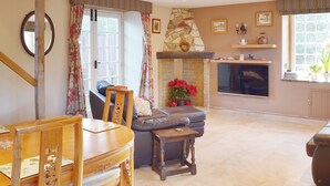 A living room with a fireplace, a dining area with a wooden table and chairs, and a stone accent wall. - 1 bedroom accommodation in Brighstone, near Yarmouth (Brighstone, near Yarmouth)