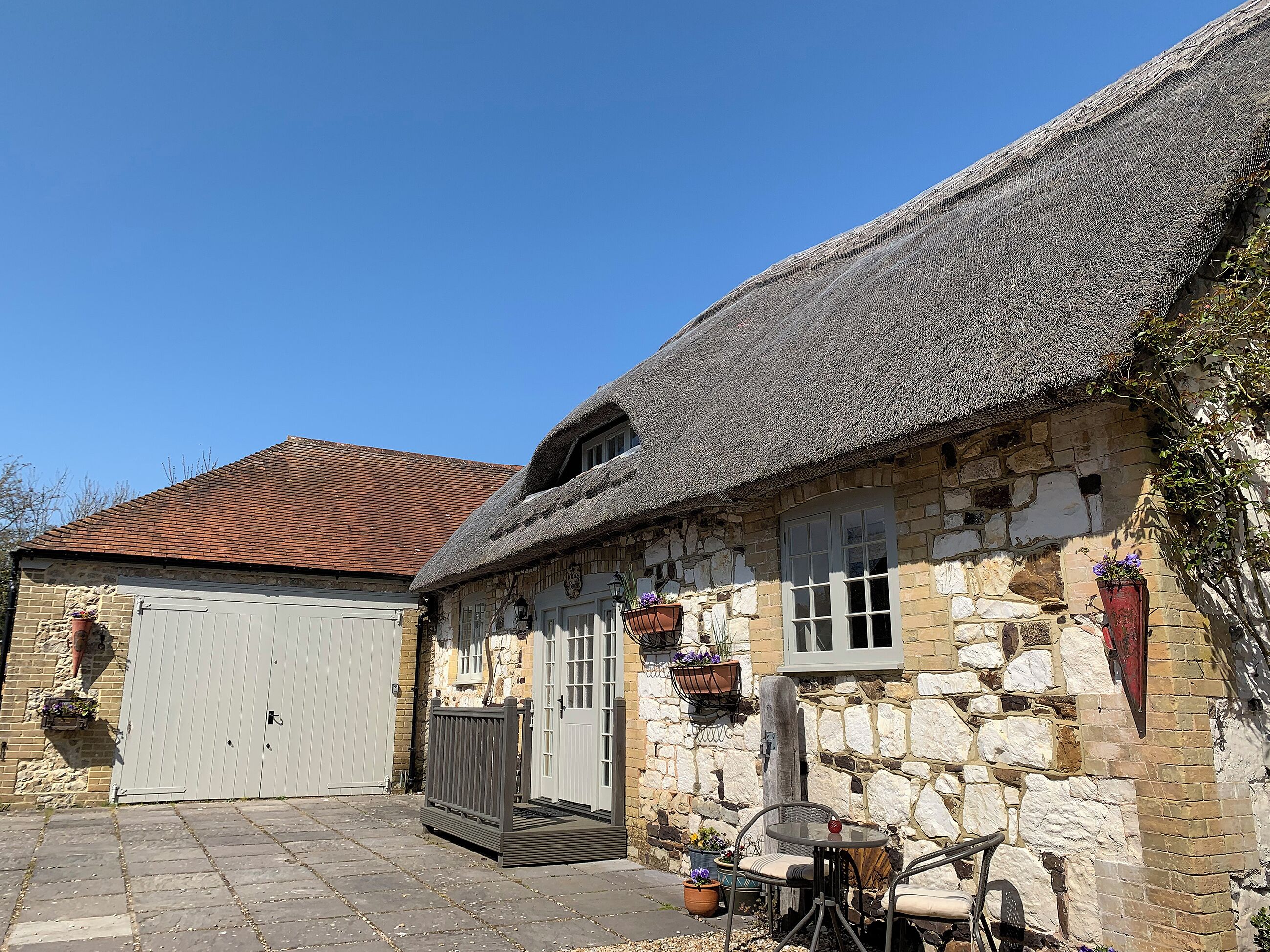 A stone building with a thatched roof, a wooden door, and a small table with chairs outside.