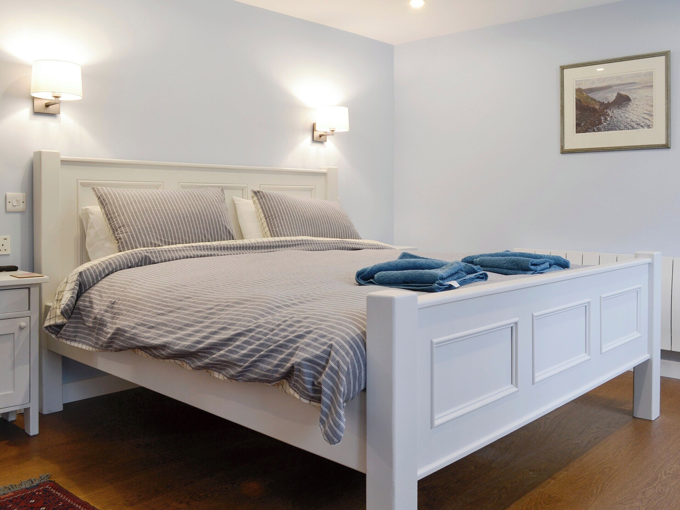 A neatly made bed with a striped bedspread and pillows, a bedside table with a lamp, and a framed picture on the wall.