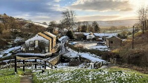 Un pueblo rural con caminos y edificios cubiertos de nieve, un puente y un paisaje montañoso.