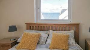 A bedroom with a wooden headboard, a window with a view of the sea, and patterned bedding. - 2 bedroom accommodation in Portmahomack, near Tain (Portmahomack, near Tain)