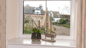 A window with a model sailboat and a potted plant on the sill. - 2 bedroom accommodation in Portmahomack, near Tain (Portmahomack, near Tain)