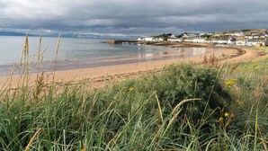 A coastal landscape with a sandy beach, grassy foreground, and a row of white houses along the shore. - 2 bedroom accommodation in Portmahomack, near Tain (Portmahomack, near Tain)