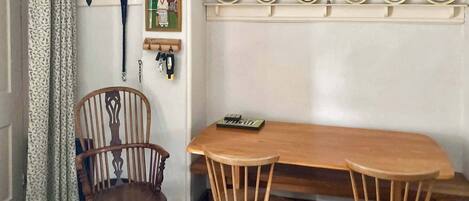 Un comedor con una mesa de madera y dos sillas, un perchero con llaves, y una estantería con platos decorativos.