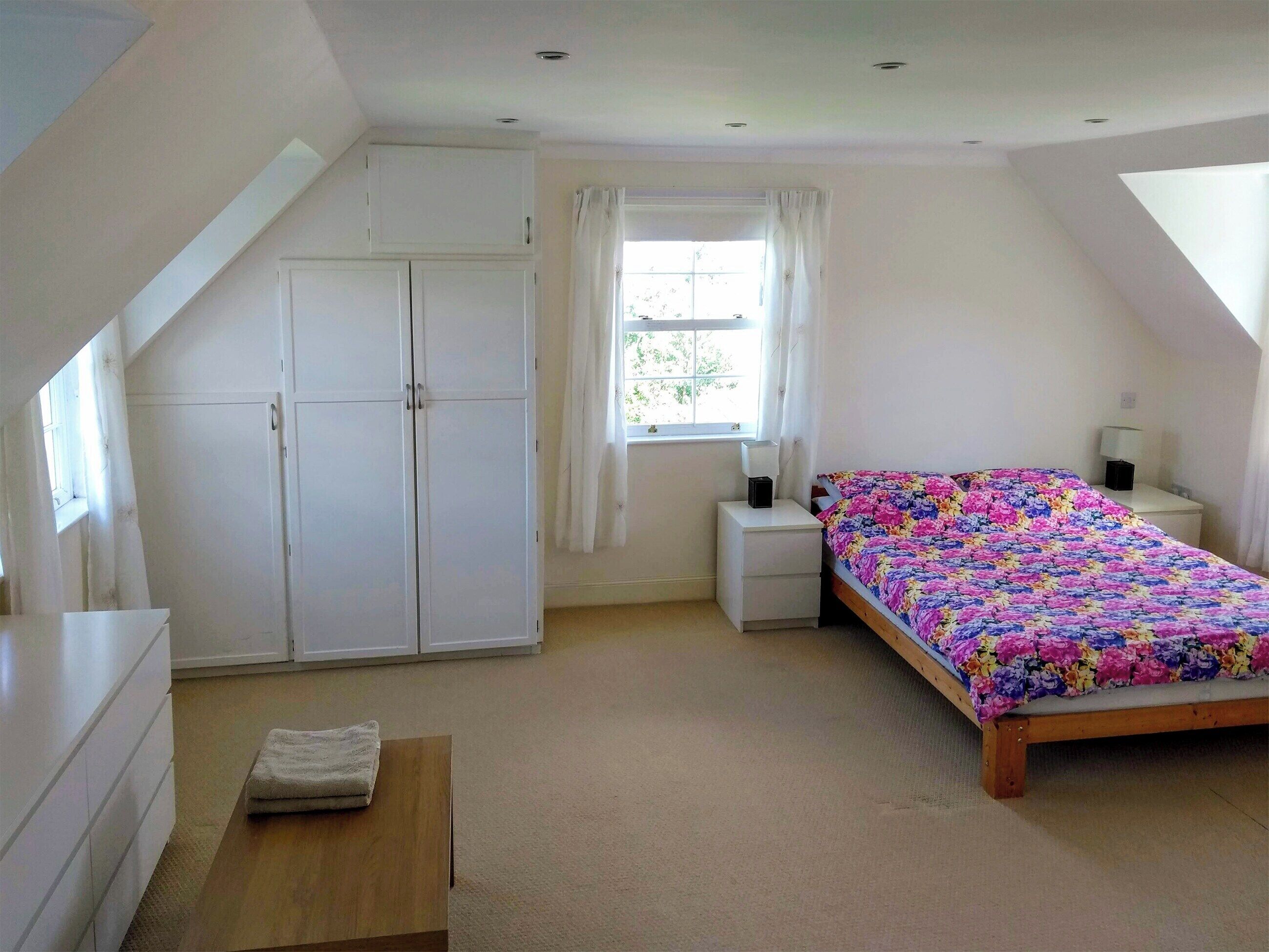 Une chambre à coucher avec un lit, un bureau, une armoire et une fenêtre avec des rideaux.
