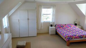 Een slaapkamer met een bed, een bureau, een kledingkast en een raam met gordijnen.