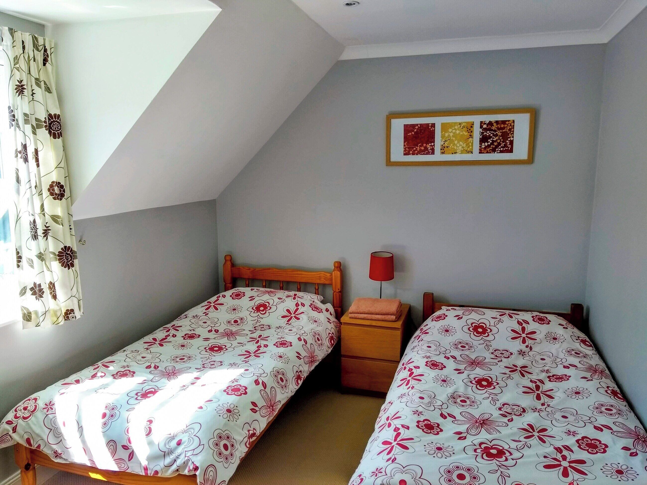 Ein Schlafzimmer mit zwei Einzelbetten, einem Nachttisch, einer roten Lampe und einem gerahmten Bild an der Wand.