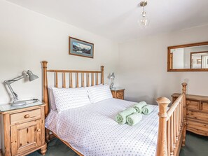 A neatly made bed with a patterned bedspread, a wooden headboard, two bedside lamps, a wooden nightstand, and a mirror on the wall.