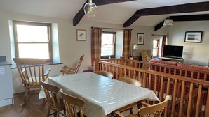 Zona pranzo con tavolo e sedie in legno, televisione e finestra con tende.