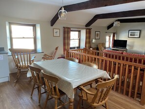 A dining area with a wooden table and chairs, a TV, and a window with curtains.