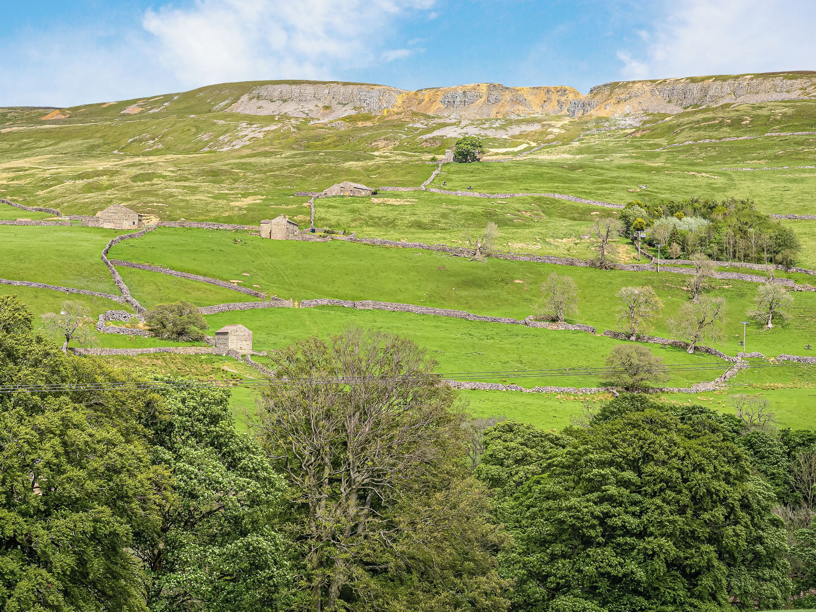 A rural landscape with stone walls and traditional stone buildings, likely a farmstead or small village.