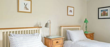 Una habitación con dos camas individuales, cabeceros de madera, mesitas de noche con lámparas y cuadros enmarcados en las paredes.