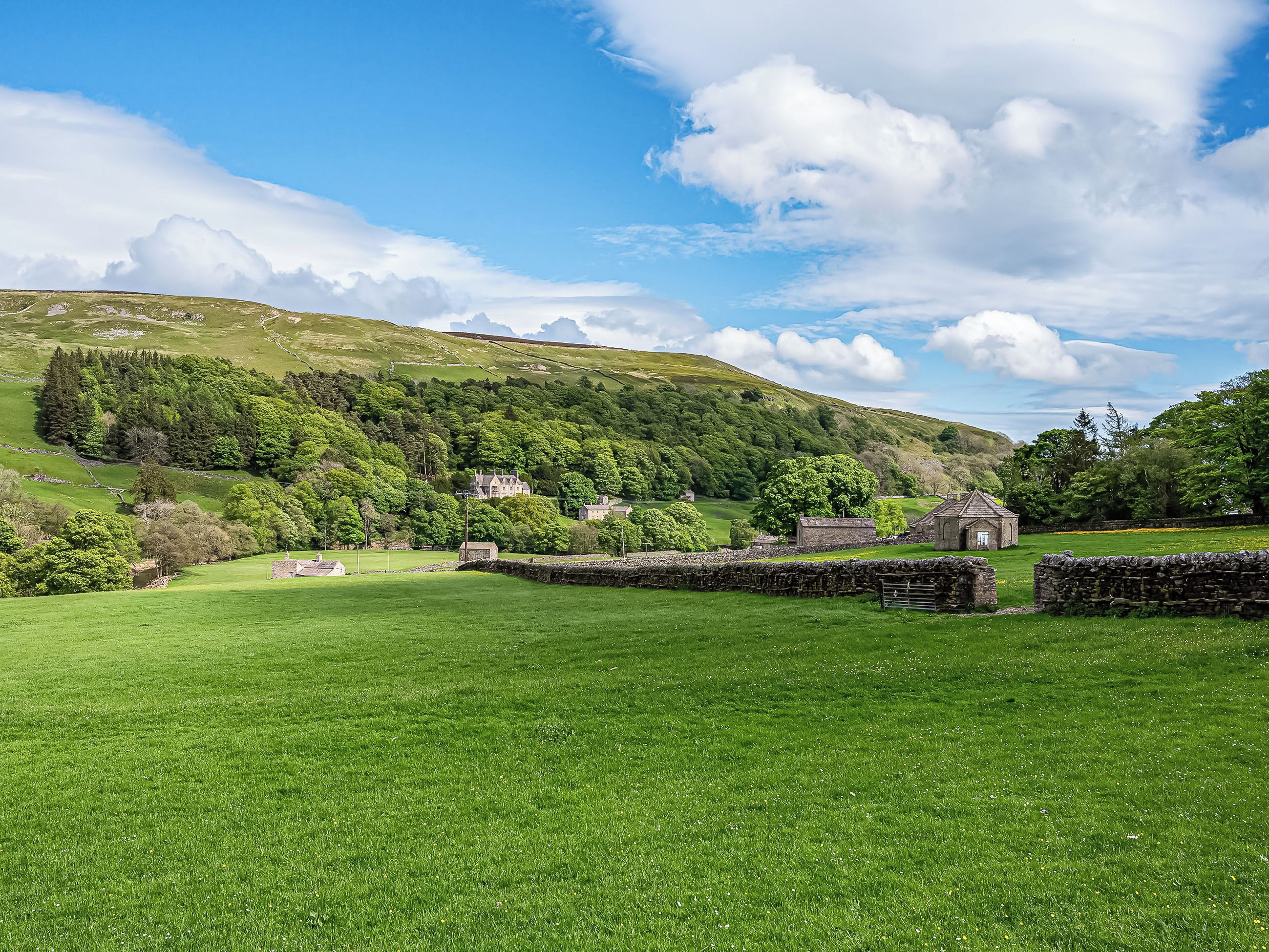 A rural landscape with rolling hills, a stone wall, and traditional stone buildings.