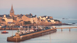 Un pueblo costero con edificios históricos, una torre destacada y un puerto con barcos.