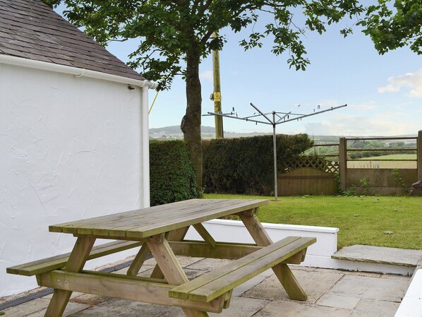 A wooden picnic table in a backyard with a white building and a hedge in the background. - Deuglawdd Cottage - HW7788 (Aberdaron, near Pwllheli)