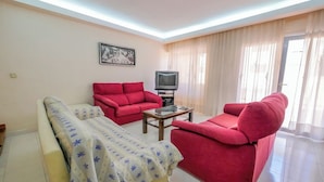 A living room with a sofa set, a television, and a bed.