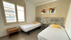 A room with two beds, a wooden nightstand, and a window with blinds.