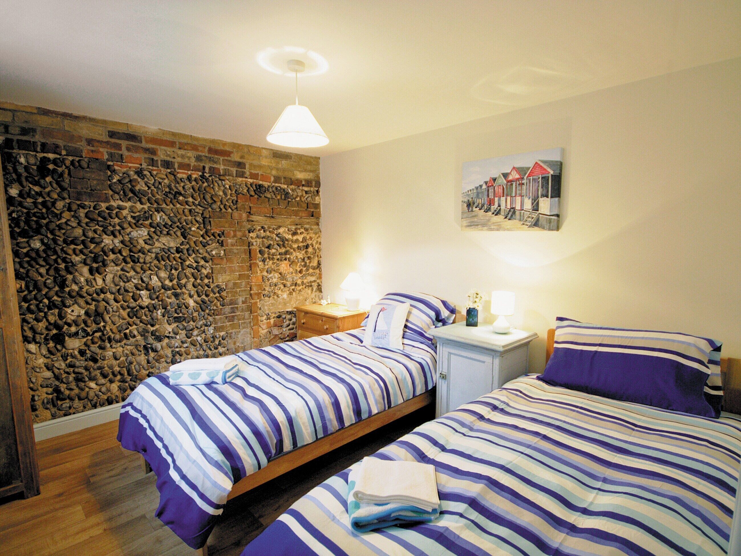 Une chambre avec deux lits, un mur en pierre, un plancher en bois et un tableau accroché au mur.