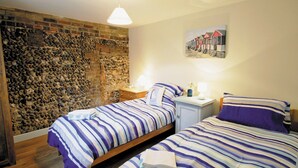 Una camera da letto con due letti, un muro in pietra, un pavimento in legno e un quadro appeso al muro.