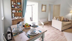 Zona pranzo con tavolo in legno apparecchiato per quattro persone, una ciotola di frutta e una credenza con diversi piatti.