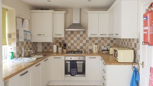 A compact kitchen with white cabinets, a tiled backsplash, a stove, a microwave, and a sink. - 2 bedroom accommodation in Bridlington (Bridlington)