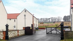 A gated entrance to a residential area with a stone wall, a lamp post, and a red-tiled roof building. - 2 bedroom accommodation in Bridlington (Bridlington)