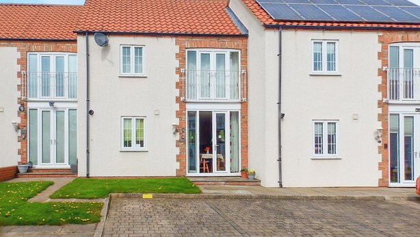 A two-story residential building with a red-tiled roof, white-framed windows, and a solar panel on the roof. - 2 bedroom accommodation in Bridlington (Bridlington)