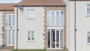A two-story residential building with a balcony, a sliding glass door entrance, and a small garden area. - 2 bedroom accommodation in Bridlington (Bridlington)