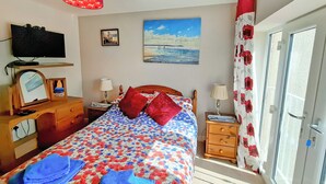 A bedroom with a bed, bedside tables, a TV, a painting, and a window with curtains. - 2 bedroom accommodation in Bridlington (Bridlington)