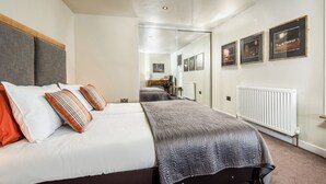 Un dormitorio con cama, mesita de noche, espejo y cuadros en la pared.