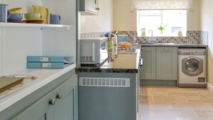 Une cuisine avec des armoires bleu clair, un four à micro-ondes encastré, un lave-vaisselle et une fenêtre donnant sur l’extérieur.