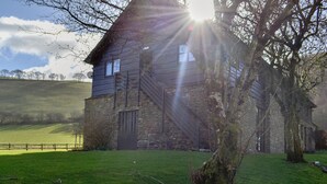 A rustic stone building with a wooden staircase leading to a second floor, surrounded by a grassy field and trees. - 1 bedroom accommodation in Newbridge-on-Wye, near Builth Wells (Newbridge-on-Wye, near Builth Wells)