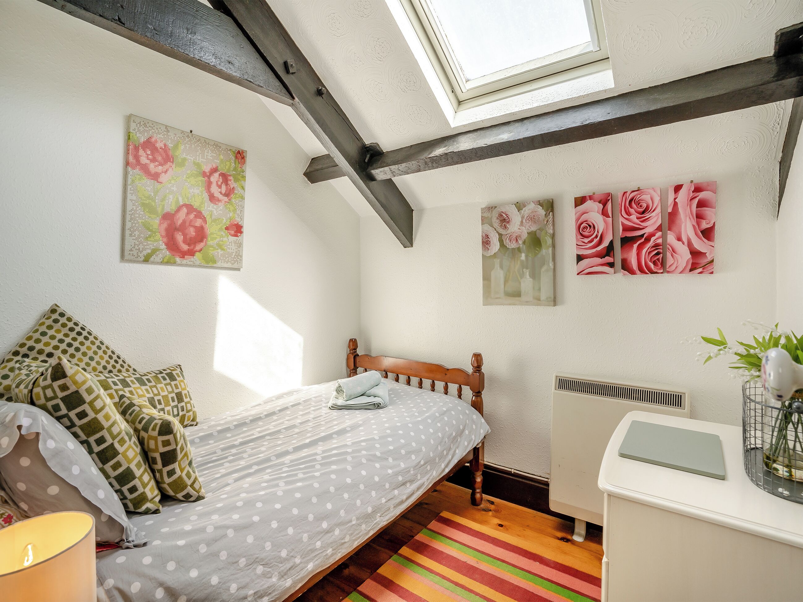Un dormitorio con cama, radiador, tragaluz y decoración floral en la pared.