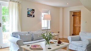 A living room with a sofa, a coffee table with magazines, a lamp, and a door. - A detached character cottage with beams, wood burner and enclosed garden. (Nanternis near New Quay)