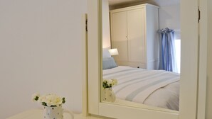 A bedroom with a bed, a nightstand, a mirror, and a vase with flowers. - A detached character cottage with beams, wood burner and enclosed garden. (Nanternis near New Quay)