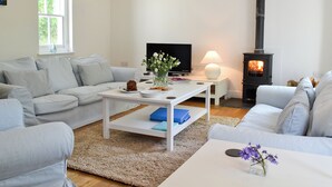 A living room with a sofa, a coffee table, a TV, a lamp, and a fireplace. - A detached character cottage with beams, wood burner and enclosed garden. (Nanternis near New Quay)