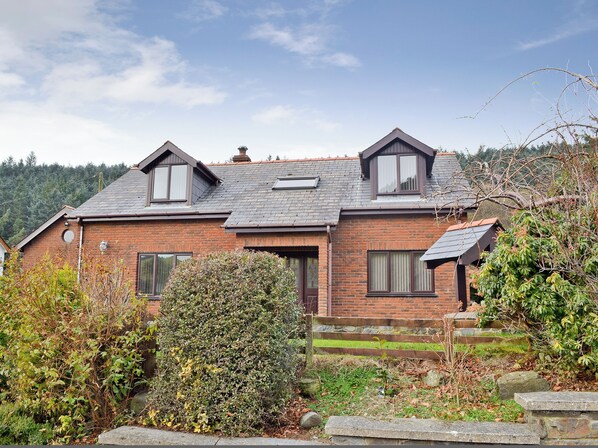 A two-story brick house with a sloped roof, dormer windows, and a stone staircase leading to the entrance.