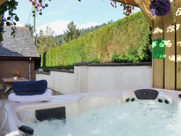 A hot tub with water, a wooden structure, and a wall with greenery.