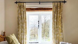 Ein Schlafzimmer mit Bett, einem Fenster mit Vorhängen und Blick auf Bäume.