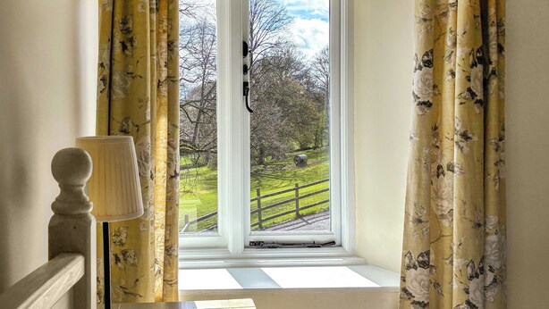 Ein Zimmer mit Fenster, Vorhängen, einer Lampe und Blick auf eine grüne Landschaft mit einem Zaun.