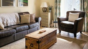 Ein Wohnzimmer mit Ledersofa, Holzschrank, Beistelltisch mit Lampe und Sessel.