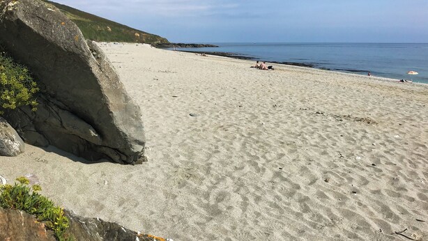 Una spiaggia con una scogliera rocciosa da un lato e un cielo sereno.