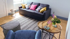 A living room with a dark grey sofa, patterned rug, and a round wooden coffee table with a vase of flowers.