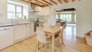 A modern kitchen with white cabinets, a wooden ceiling, and a dining area with wicker chairs and a wooden table. - 2 bedroom accommodation in Swainby, near Stokesley (Swainby, near Stokesley)