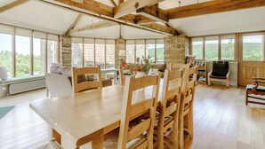 A spacious room with a high ceiling, wooden beams, a large dining table, and multiple chairs. There is a stone wall and large windows providing a view of the outdoors. - 2 bedroom accommodation in Swainby, near Stokesley (Swainby, near Stokesley)