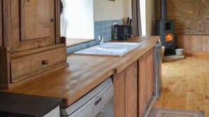 Une cuisine avec des meubles en bois, un lave-vaisselle, un évier et un mur en pierre agrémenté d’une cheminée.