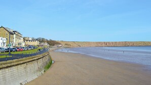 Une ville côtière dotée d’une plage de sable, d’une promenade bordée de voitures garées et d’immeubles le long du littoral.