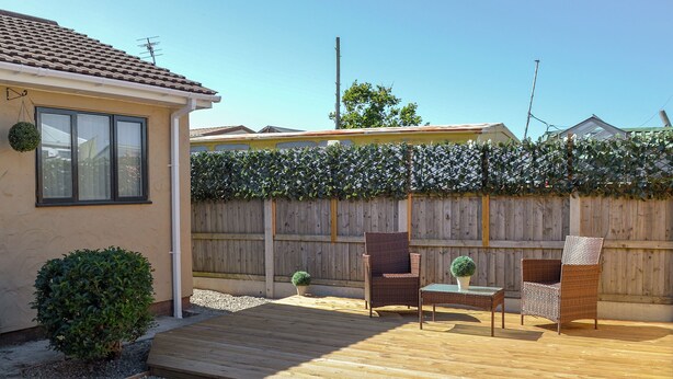 A wooden deck with two wicker chairs and a small table, surrounded by a wooden fence and a hedge. - 1 bedroom accommodation in Towyn, near Rhyl (Towyn, near Rhyl)